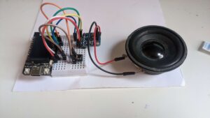 A picture of the testing setup. A TTGO T-Display ESP32 development board plugged into a breadboard, wired to a button and amplifier, which is in turn wired to a small speaker.